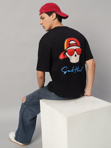 Back View – SMOKHEAD Men's Oversized Black T-Shirt with Bold Skull Graphic Wearing Cap and Sunglasses